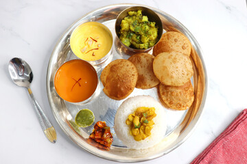 Indian vegetarian Thali or platter includes Aloo ki sabji, dal rice, Puri bhaji, Shrikhand or Srikhand, Aamras, papad, pickle, and chutney. Indian food is served in a Silverplate or thali. Copy Space.