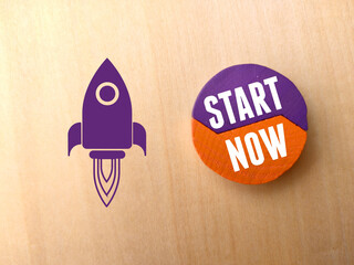 Colored block and icon with text START NOW on wooden background.
