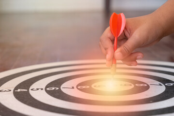 The hand holding the dart is aimed at the specified target. The concept of accuracy in finding the target audience. - obrazy, fototapety, plakaty
