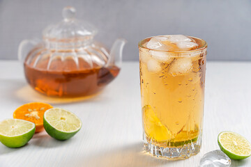 Homemade organic fresh iced tea in tall drinking glass with ice cubes and slices of sour lime and...