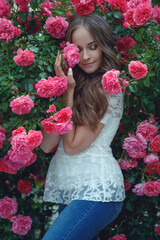 Beautiful portrait of a woman in poses. A brunette woman is standing next to roses in nature.