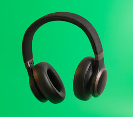 Black audio headphones isolated on green background.