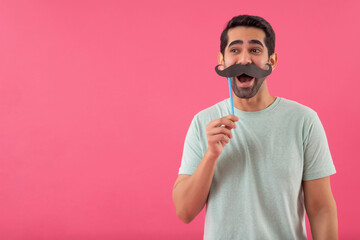 Portrait of  funny young man holding fake mustache and looking elsewhere