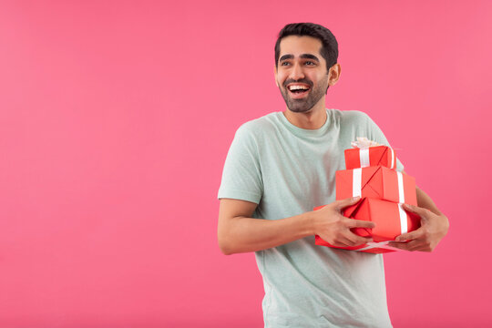 Happy young man holding gifts in his hands against pink background