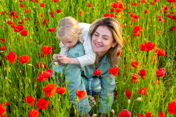 Mom with a child girl in a field of red poppies enjoys nature. Mother and little daughter in the poppy field. Mother and daughter on spring.