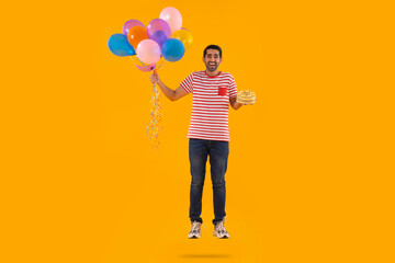 Happy young man flying with air balloons with cake in hand