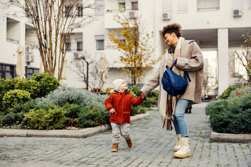 A playful babysitter holding hands with the little boy and taking him to the daycare or pre-school. - obrazy, fototapety, plakaty