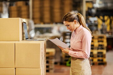 A female warehouse worker doing paperwork and controlling shipment.