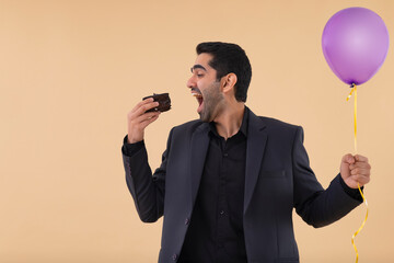 Naklejka premium Portrait of happy businessman holding balloon in one hand and eating cake with other