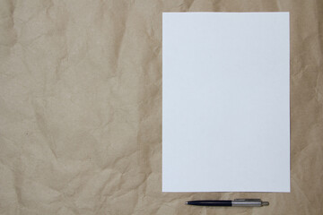 White empty sheet of A4 format with pen on a beige craft paper. Concept of analysis, study, attentive work. Stock photo with empty place for your text and design.