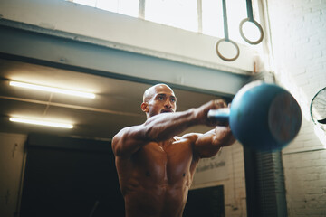 Total body power. Low angle shot of a muscular young man exercising with a kettlebell in a gym.