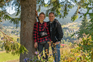 A happy tourist is standing in a shade and smiling in the mountains, near a small village