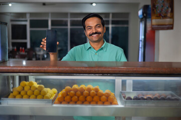 Sweet shop owner displaying Smartphone while standing at counter