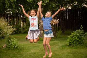 Girls 10 years old jump on the grass in the summer in hands holding flowers.