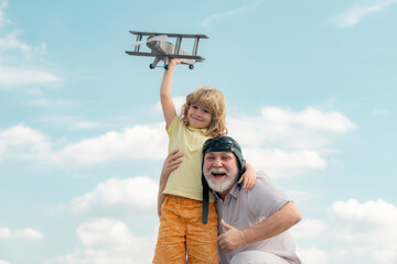 Old grandfather and young child grandson playing with plane together on blue sky. Cute boy with granddad playing outdoor.