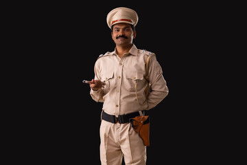 Portrait of an Indian policeman standing with baton and hand behind back