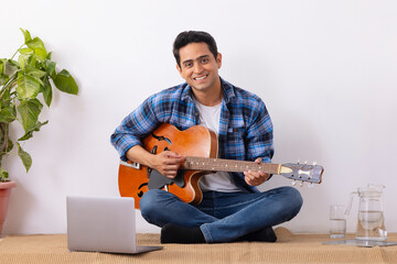 Young music teacher running an online guitar class in living room