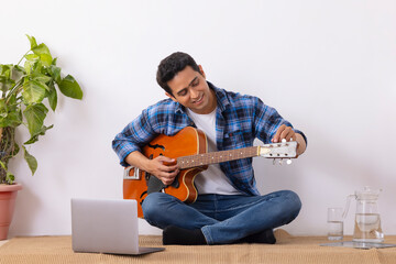 Young music teacher tuning guitar during online class in living room