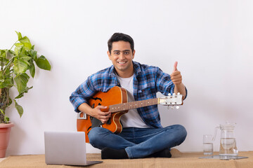 Young music teacher showing perfect symbol during online guitar class in living room