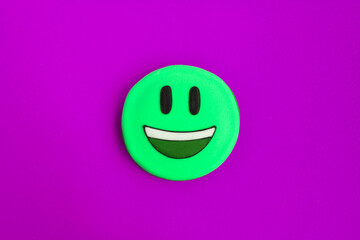 Green smiley in the form of gingerbread on the purple background. Closeup. Copy space.