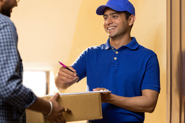 Young delivery boy requesting customer to sign receipt after receiving parcel
