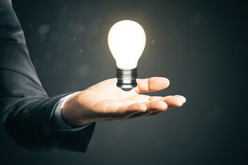 Close up of businessman hand holding glowing light bulb. Idea and innovation concept.