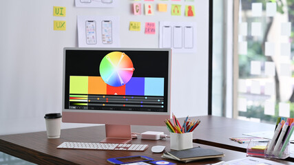 Design studio with computer, color swatches and wireframe sketches for mobile application on wooden...