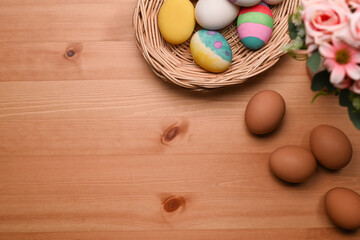 Colorful Easter eggs in wicker basket and spring flowers on wooden background with copy space....