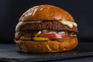 Vegan burger. Falafel and craft bun on a stone tray. Burger Veganer. Bun or lettuce, falafel, lettuce, tomato, pickled cucumber