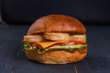 Burger with king prawns, cheese, salad, and tomato on a black wooden background.