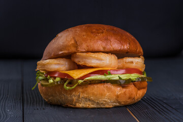 Burger with king prawns, cheese, salad, and tomato on a black wooden background.