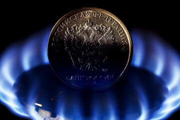 Close up of obverse of ruble coin with coat of arms of Russia on gas burner of kitchen stove. The concept of Russia selling natural gas for rubles.