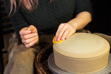 Potter's hands wipes pot with sponge close up. Woman works in pottery workshop. Clay bowl spinning on pottery wheel