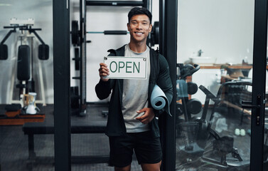 Youre welcome any time between 9 and 5. Cropped portrait of a handsome young male fitness instructor holding up a sign that says OPEN while standing in a gym.