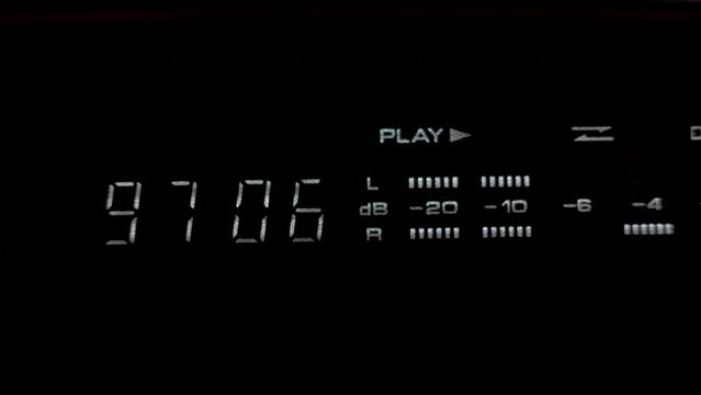 A close up shot of a digital display unit of a tape deck stereo system, the display providing a time metre and decibel reading as music is played from an old cassette