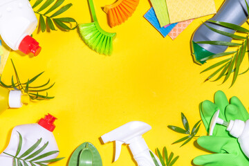 Summer cleaning concept. Plastic basket with different detergents and cleaning supplies bottles, accessories for cleaning house with palm leaves on a bright yellow background