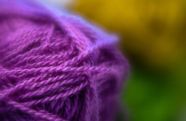 Close up of purple wool yarn. Green yellow background. Selective focus, blurred areas.