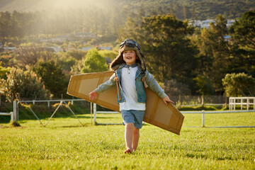 Flying on the wings of imagination. Shot of a cute little boy wearing a pilots hat and goggles while playing with cardboard wings outside.
