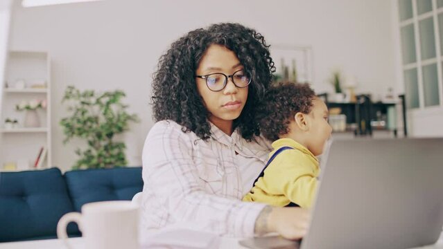 Tired African American woman working and babysitting son, unpaid maternity leave
