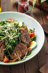 Fresh green salad with meat and quail eggs on the wooden background