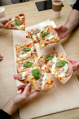  hands taking slices of slice of pizza into wooden table
