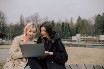 Two woman seat in the park with laptop and watch.