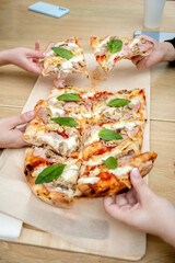  hands taking slices of slice of pizza into wooden table