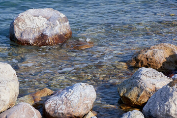 Dead Sea. Jordan. Close-up. Salt crystals on huge boulders along coast. Close-up. Stone beaches along coast of Dead Sea are washed by calm emerald waters. Calm on sea.