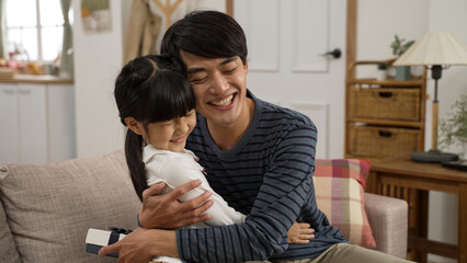 Asian girl walking towards dad and showing him surprise gift on Father’s Day at home. the touched...