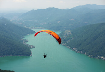 Paraglider that flies from a top of the Intelvi Valley, with a view of the Swiss Alps and Lake Lugano. Concept of lifestyle, freedom and extreme sport adventure.