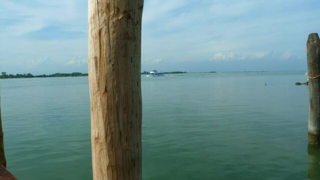 beautiful  blue green sea  inItaly, Venice, with a boat passing by and a pole in the center all in all a a beautiful sunny summer day with blue clouds pan