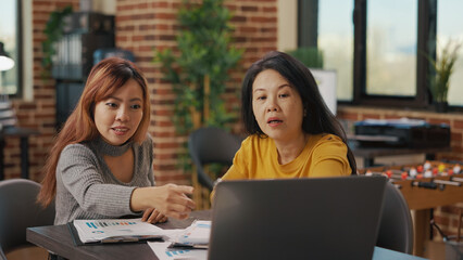 Asian women looking at laptop screen to research finance information, brainstorming ideas to plan new business strategy for development and growth. Team of people using statistics at work.