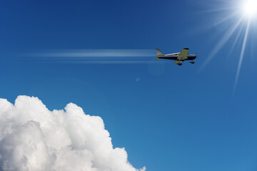 Small private propeller airplane in motion against a beautiful clear blue sky with cumulus clouds and sunbeams. - obrazy, fototapety, plakaty