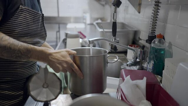 Side view of male chef filling pot with water by faucet in kitchen